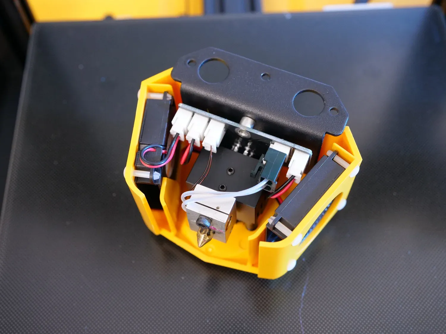 The yellow printhead shroud opened up, showing the hotend between its two blower fans