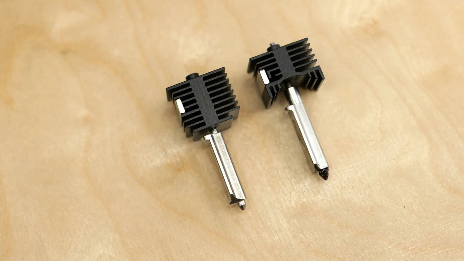 Two quick-swap hotends with their heatsinks lying on a wooden bench