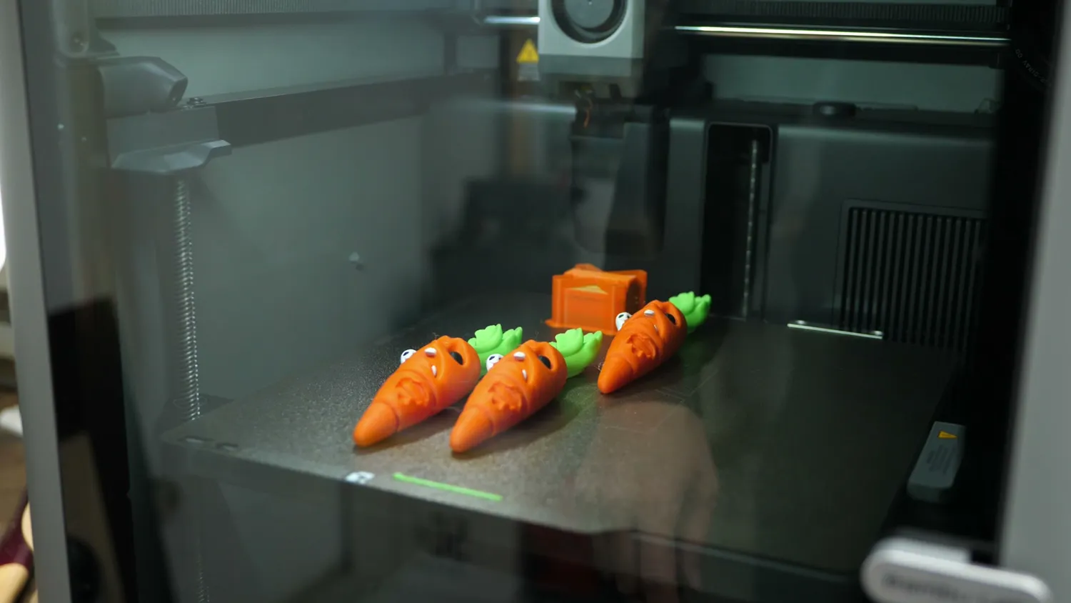 Three print-in-place flexi carrots finished on the P2S build plate
