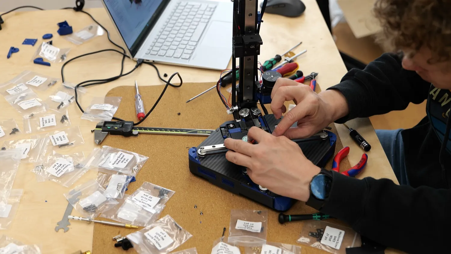 Someone assembling a small DIY 3D printer kit from bagged parts on a workbench