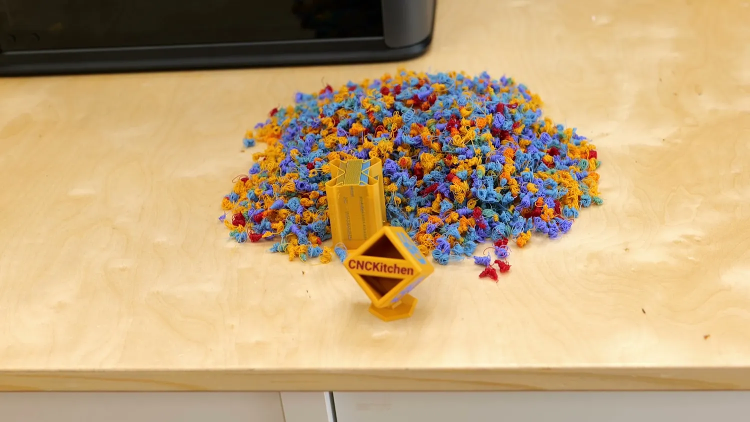 A huge pile of multicolor purge waste next to two small printed parts
