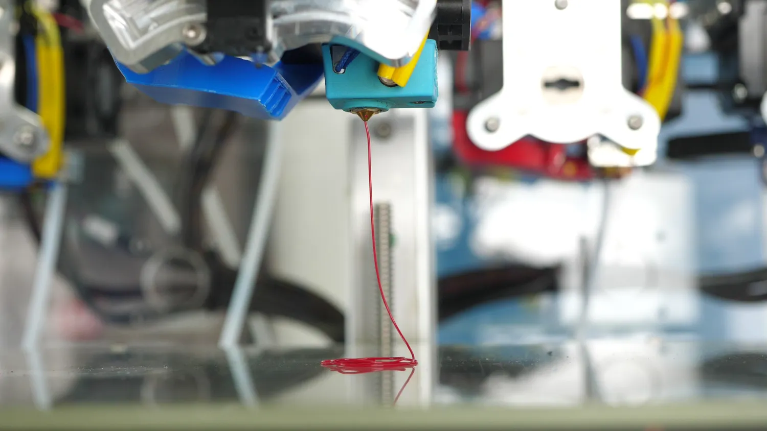 The nozzle extruding a thin, even strand of red PLA at low speed