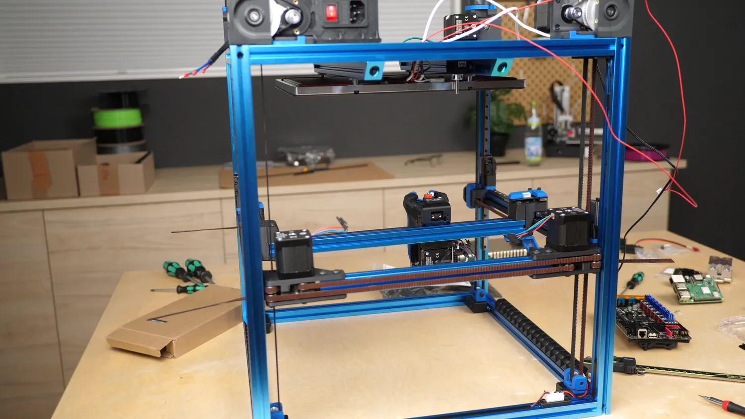 The half-built VORON 2.4 on the bench: blue frame, XY gantry with its belts and motors installed, bed hanging from the z-drives, Raspberry Pi and Octopus board still on the table
