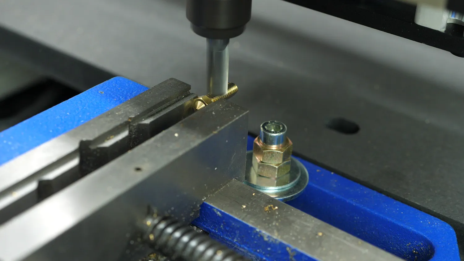 The Volcano nozzle clamped in the CNC router's vice, an end mill facing one side of the threads flat to give the cross bores a surface to start on