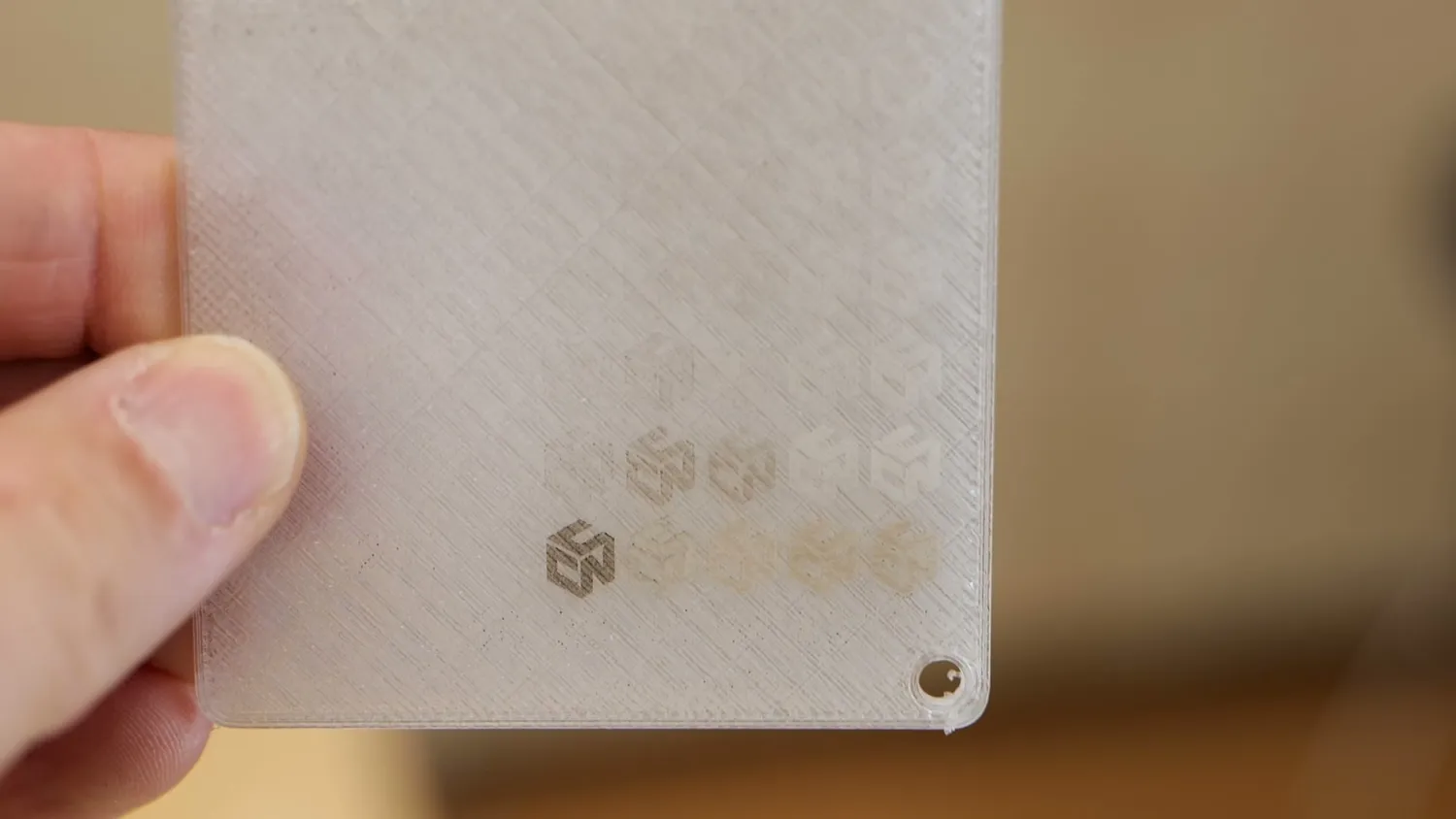Transparent 3D printed test plate held up with faint brown laser marks visible