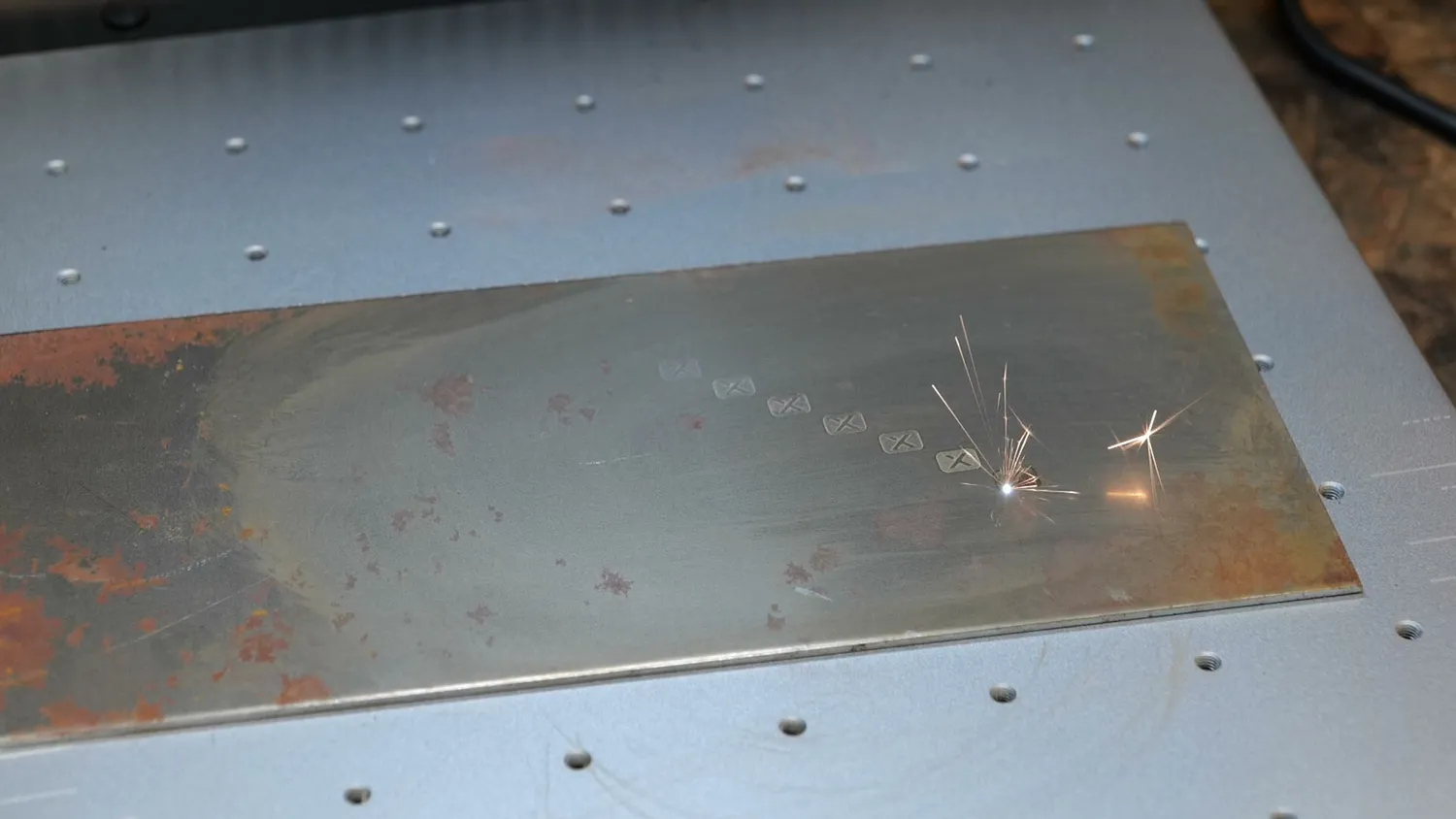 Rusty steel sheet being marked by the MOPA fiber laser with visible sparks