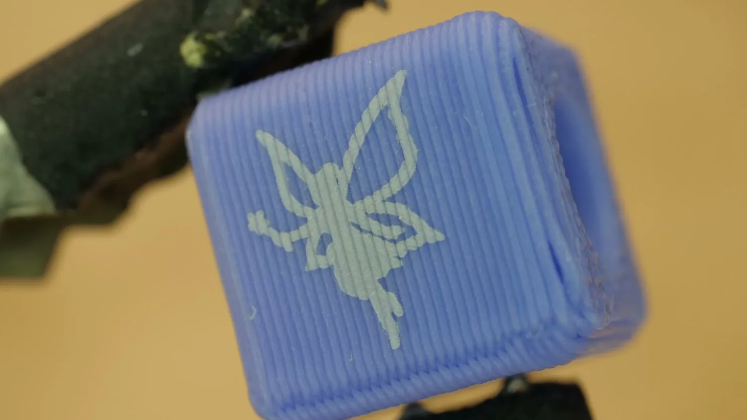 A blue PLA bracelet bead a few millimetres wide, engraved with a fairy silhouette that stays crisp at that scale