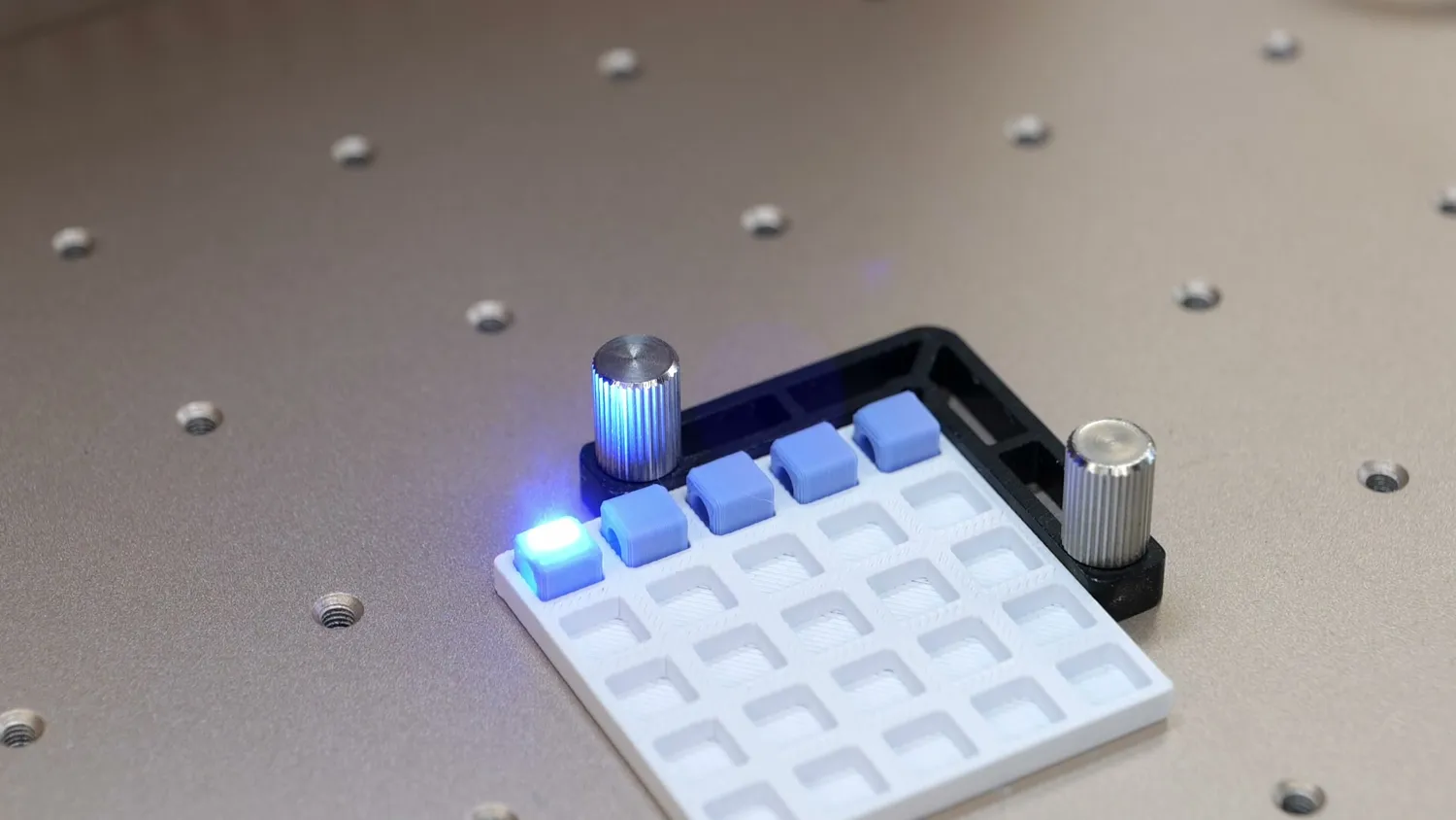 The printed fixture on the machine bed holding a row of beads against its stops, the UV laser marking the first one