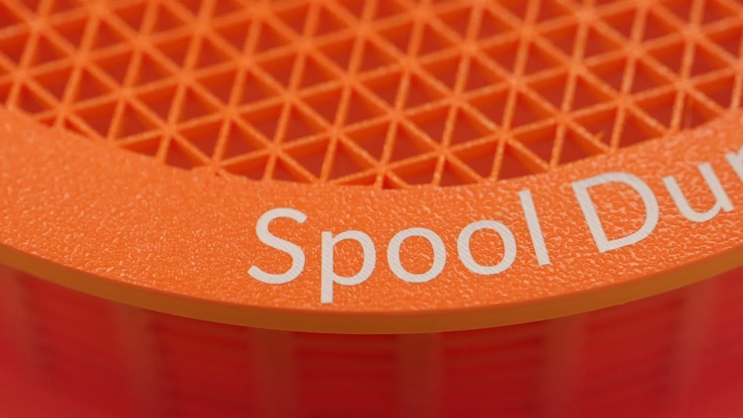 A laser-marked spool rim, the white lettering sharp against the orange plastic