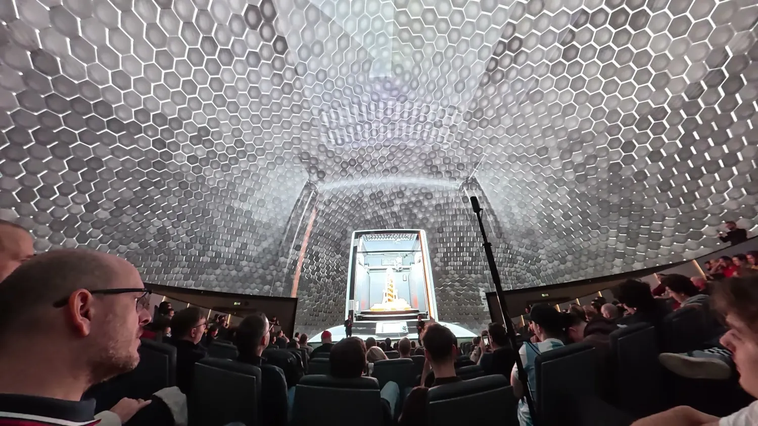 The reveal event in Prague, the audience seated inside a giant mock-up of the machine