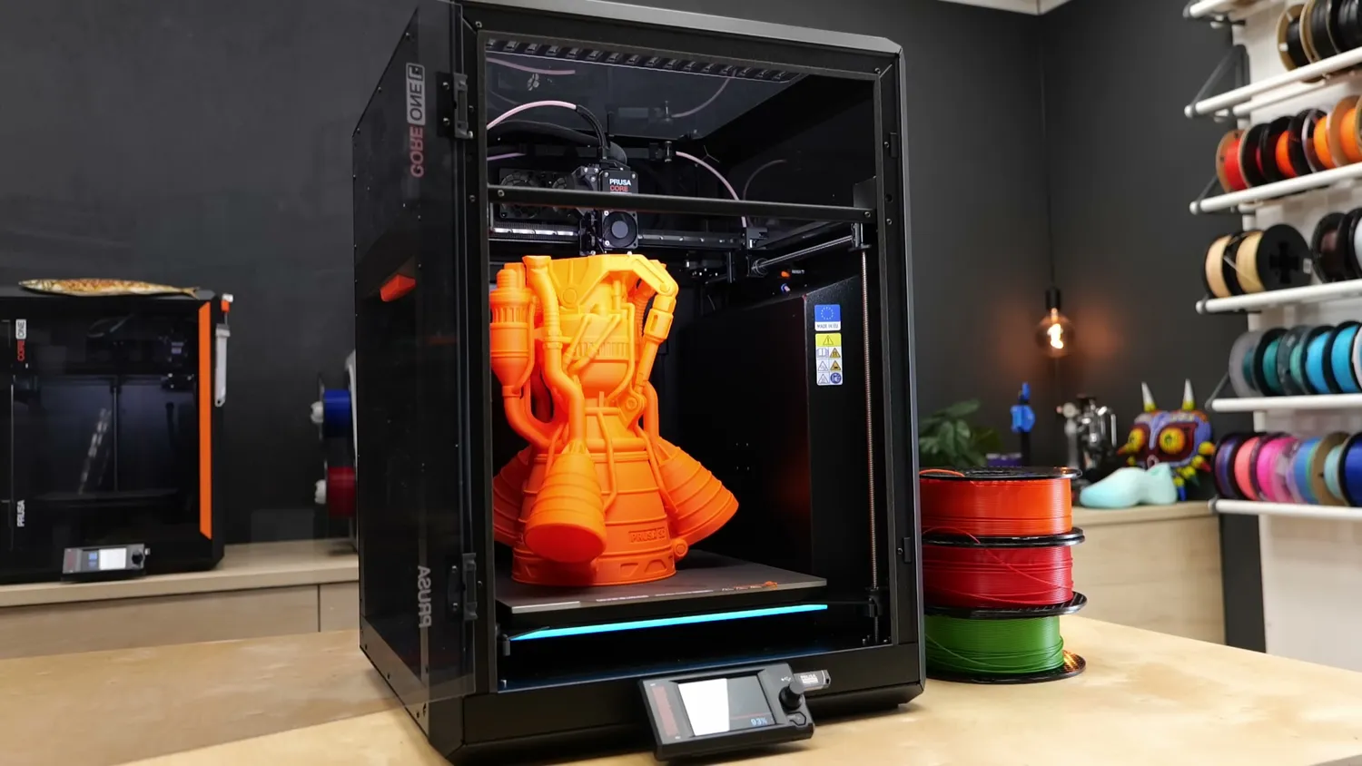 The CORE One L printing an orange model, the LED bar under the bed lit up