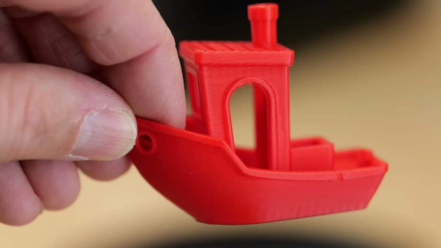 A red 3DBenchy held up to the light, faint banding visible on the lower hull
