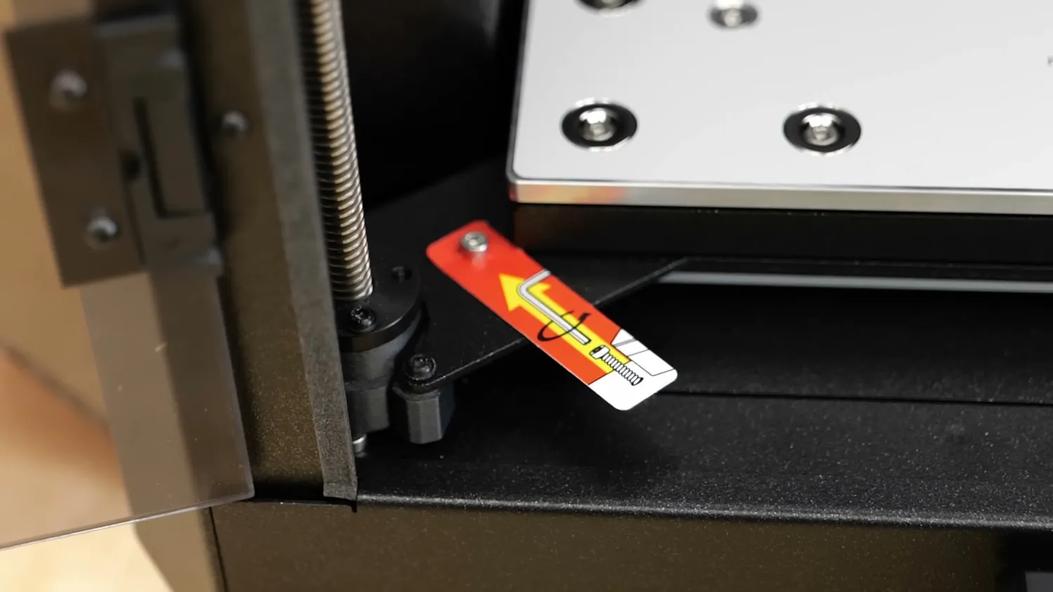 A red pull tag on one of the transport screws holding the print bed down