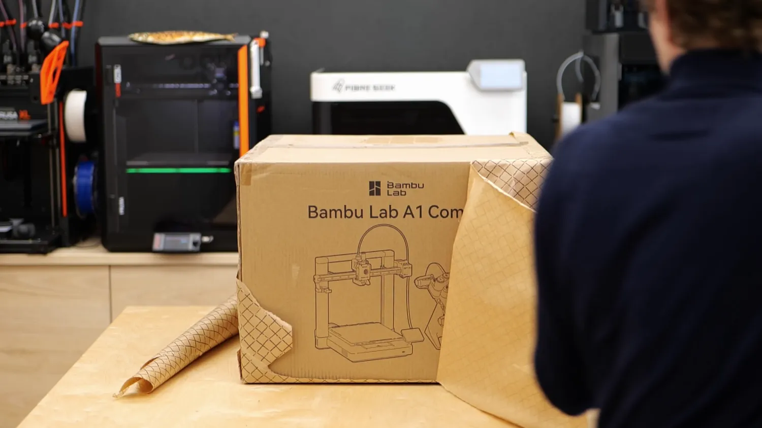 Bambu Lab A1 Combo box on the workbench in front of several 3D printers