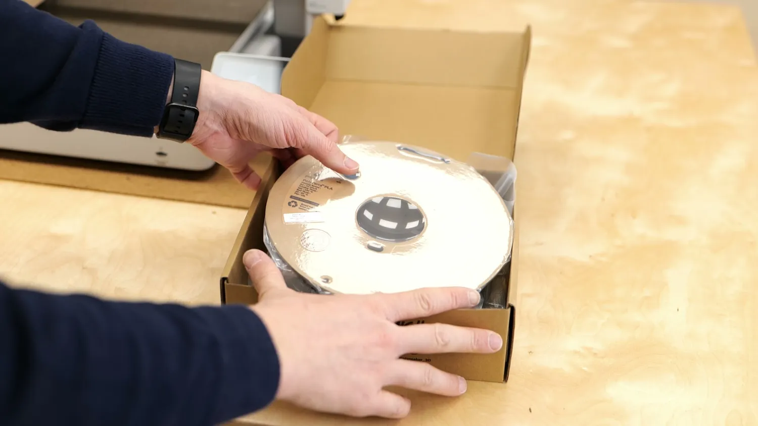 Hands unpacking a full spool of filament from its box