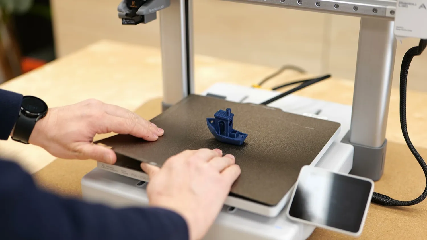 Hands lifting a freshly printed 3DBenchy off the build plate