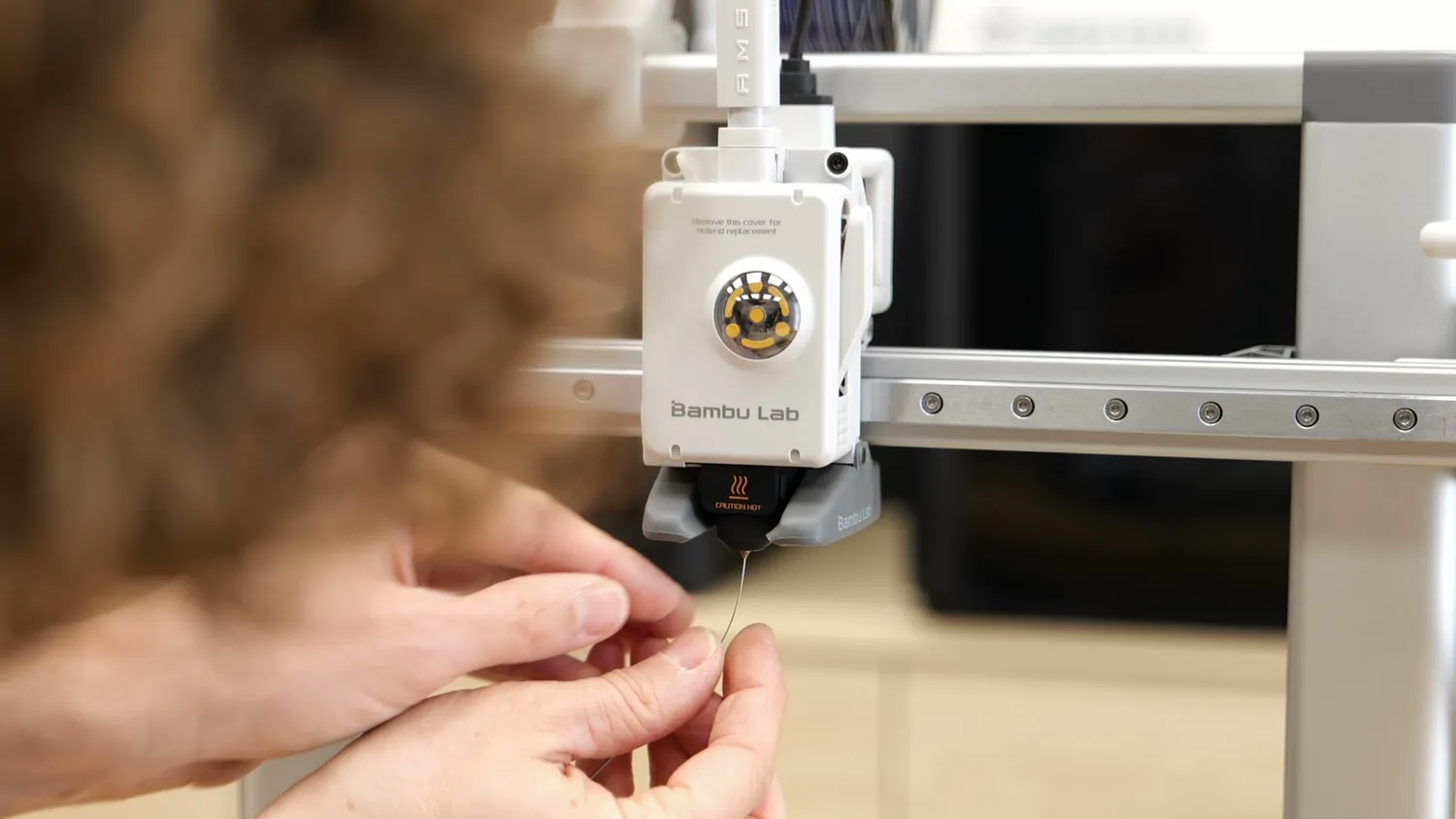 Thin cleaning wire held up to the nozzle of a 3D printer