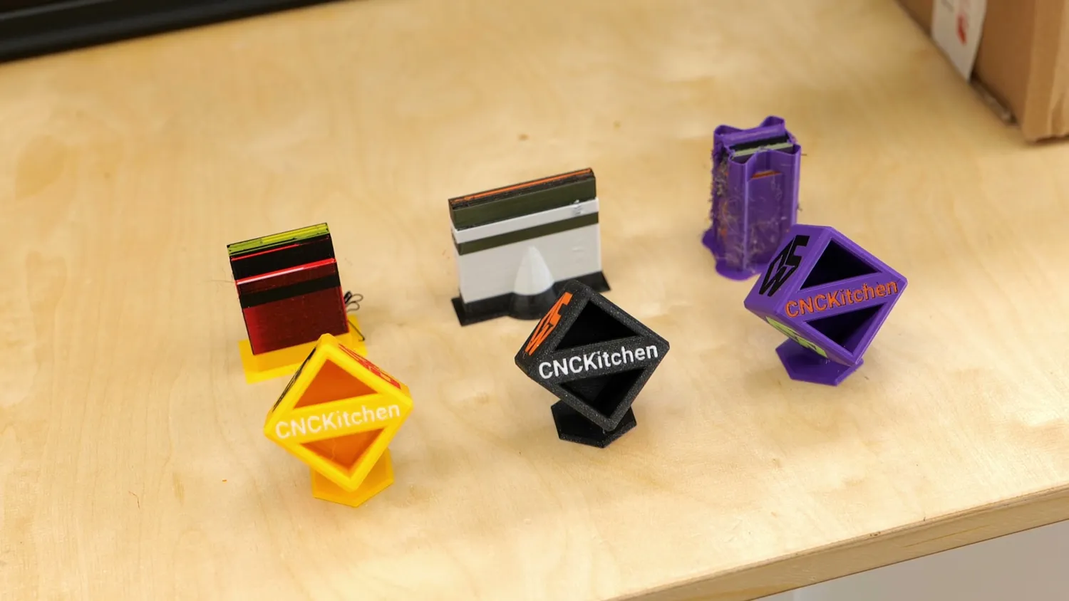 The same multi-colour cube and its prime tower printed on each machine, the purple tower on the right visibly stringier than the rest