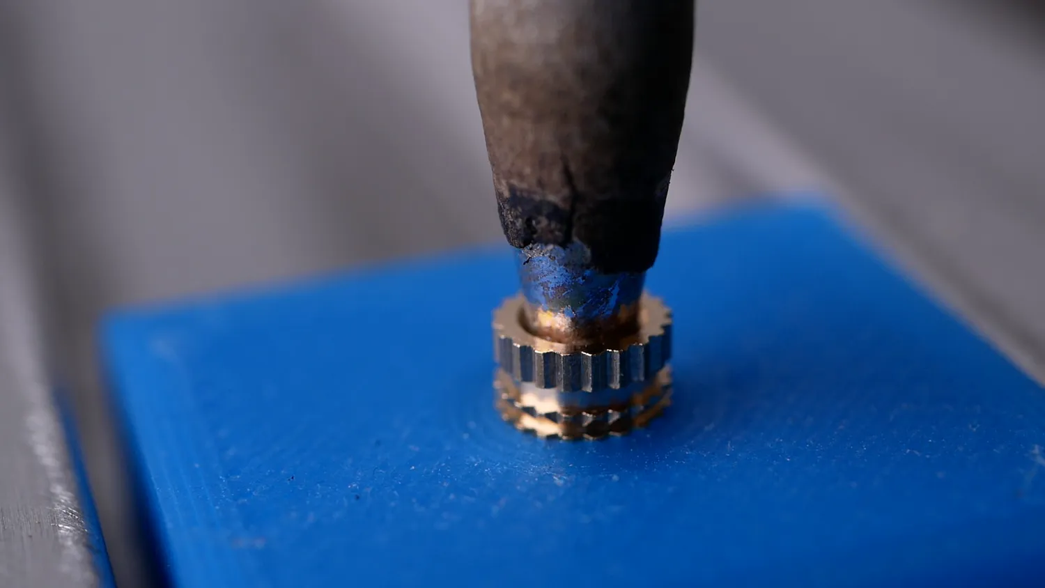 A soldering iron pressing a brass insert into a blue PLA part