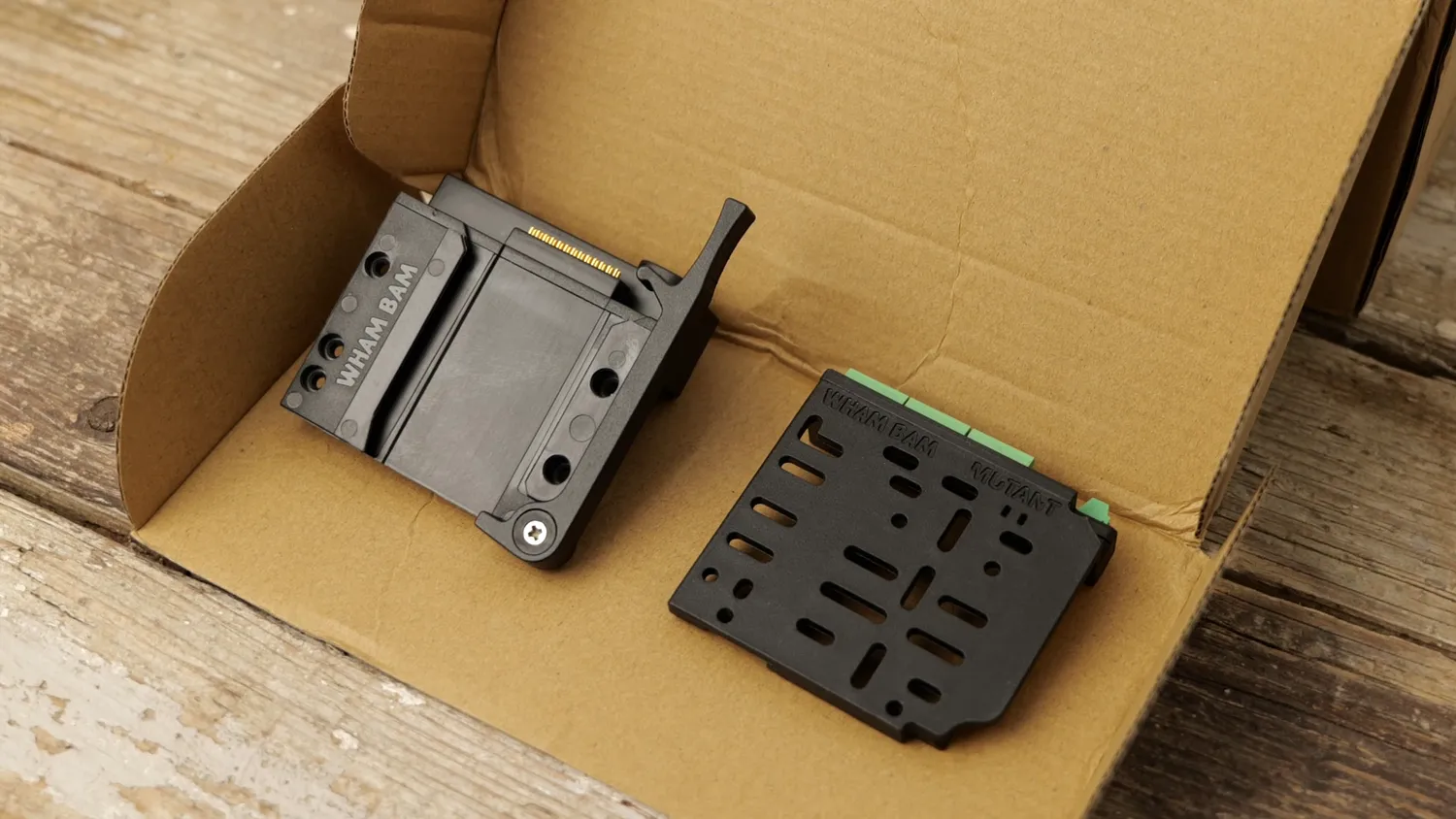 The two MUTANT plates in the box: the fixed plate with its dovetail and pogo pins, and the drilled mobile plate with green terminal blocks along the edge